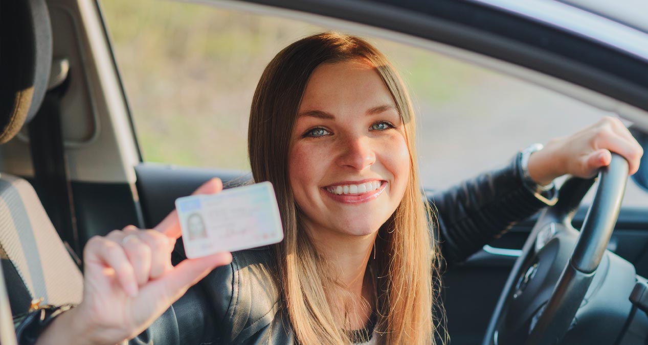 Mujer  al volante sonriendo y mostrando su licencia de manejo